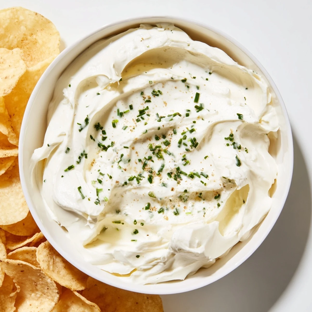 A close-up of a creamy dip bowl with chips, topped with fresh chives and parsley, ready for dipping.