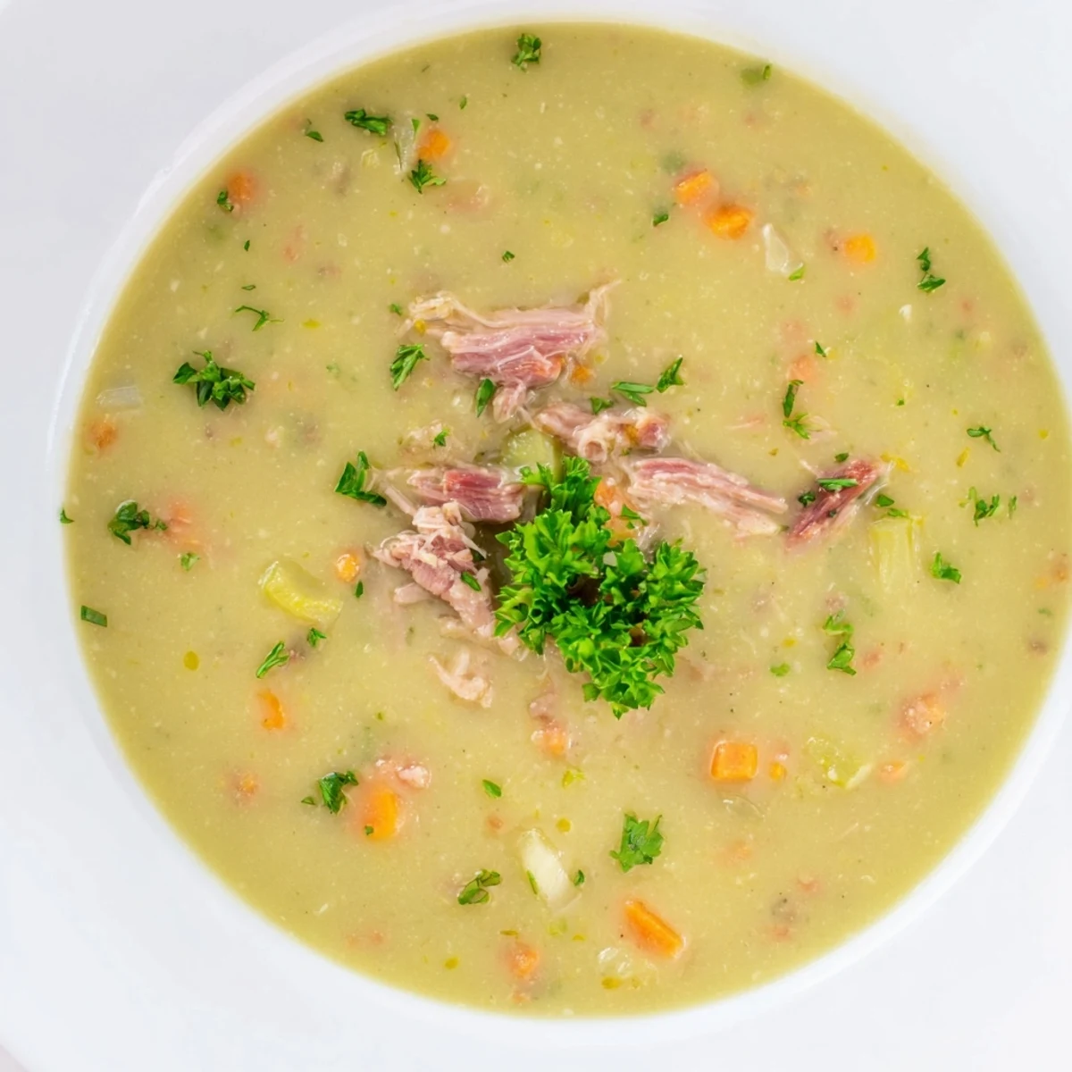 Hearty green split pea soup with smoked turkey leg, carrots, and celery in a Dutch oven, ready to serve for dinner.