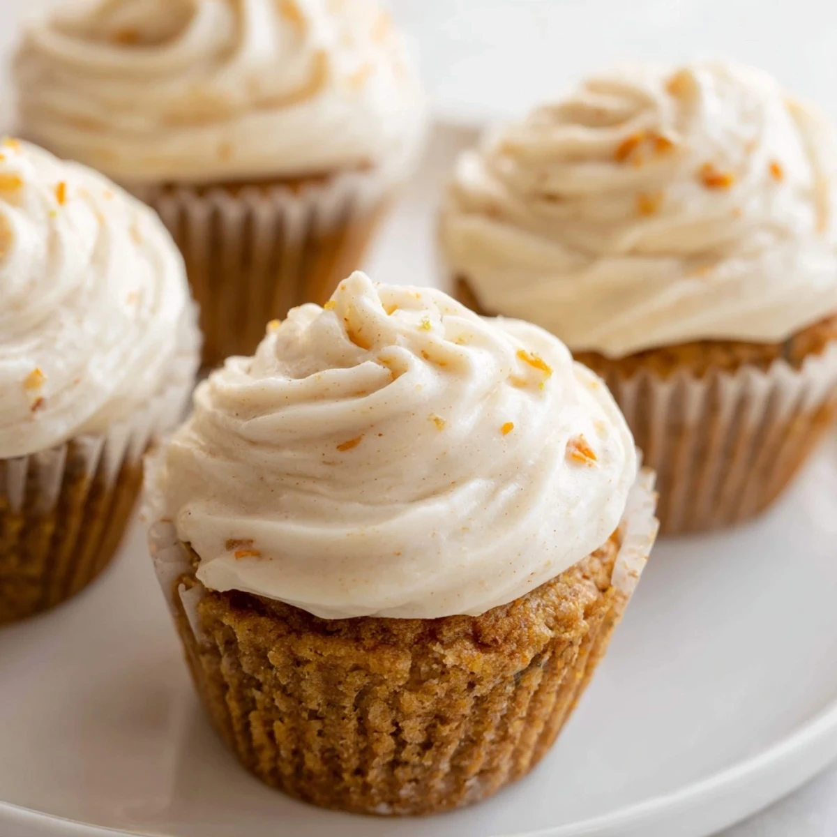 Golden-brown Carrot Cake Cupcakes topped with swirls of silky cream cheese frosting and chopped nuts.  