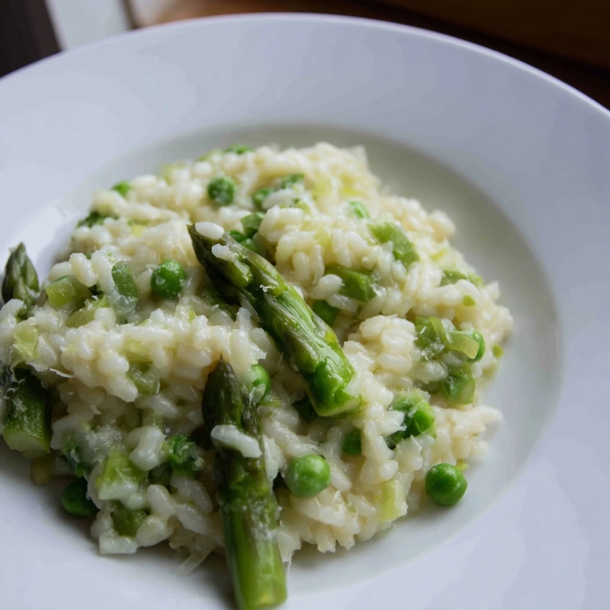 Creamy Asparagus and Pea Risotto with Parmesan steams in a pan, garnished with fresh spears and a dusting of cheese.