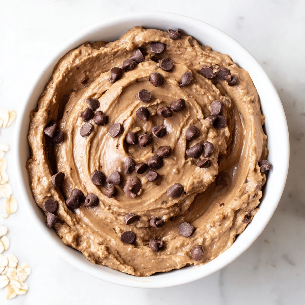 A close-up of creamy Chocolate Chip Cookie Dough Hummus topped with chocolate chips, served with fresh apple slices for dipping. 