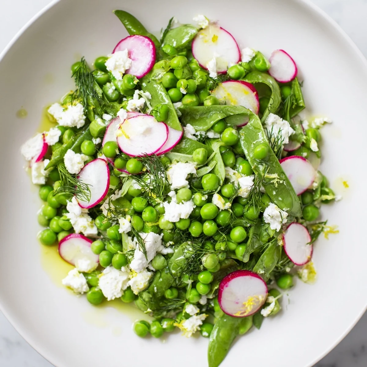 Fresh Spring Pea Salad with Radishes and Feta shown in a white bowl with lemon slices and mint leaves.