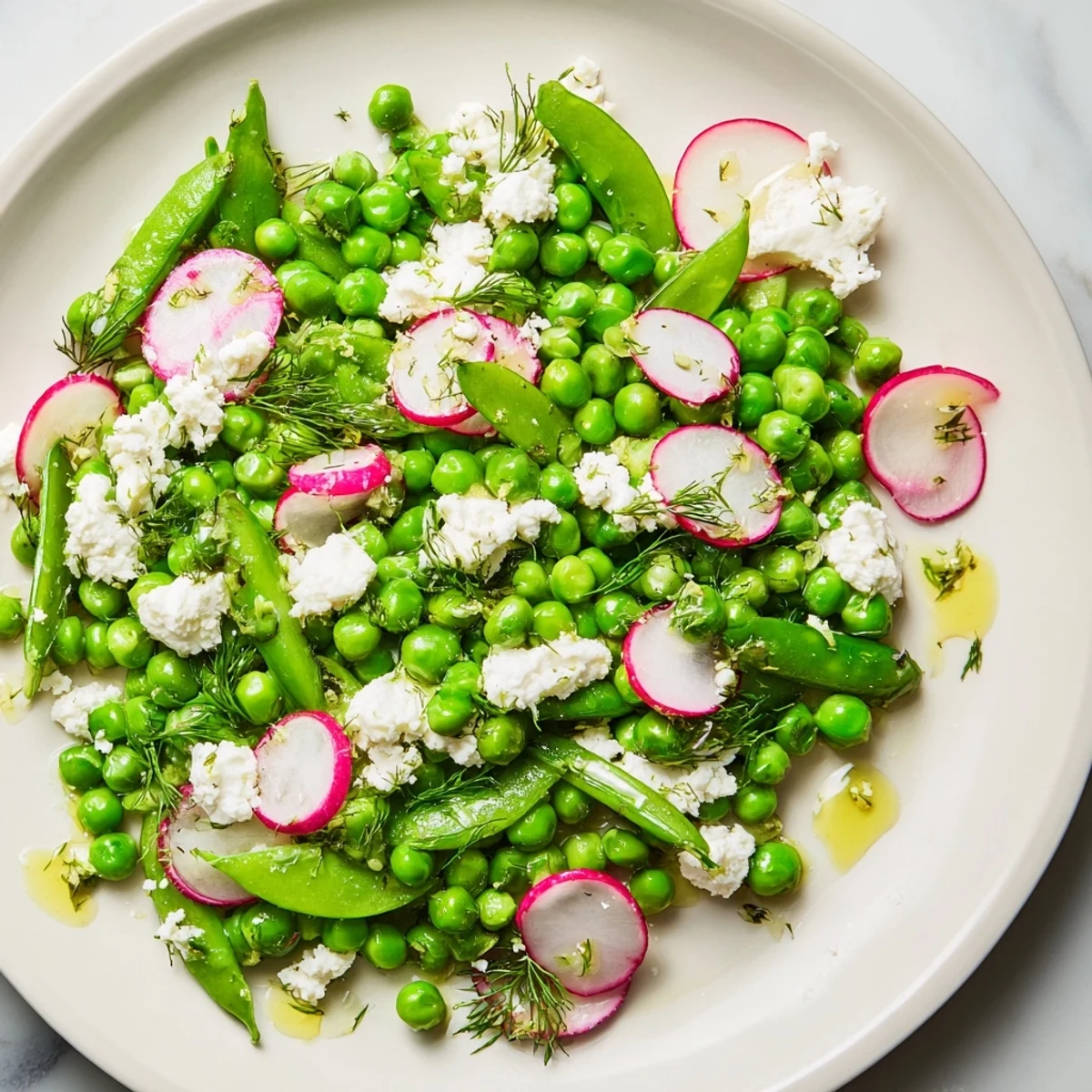 Close-up of Spring Pea Salad with Radishes and Feta on arugula, drizzled with olive oil and garnished with herbs.