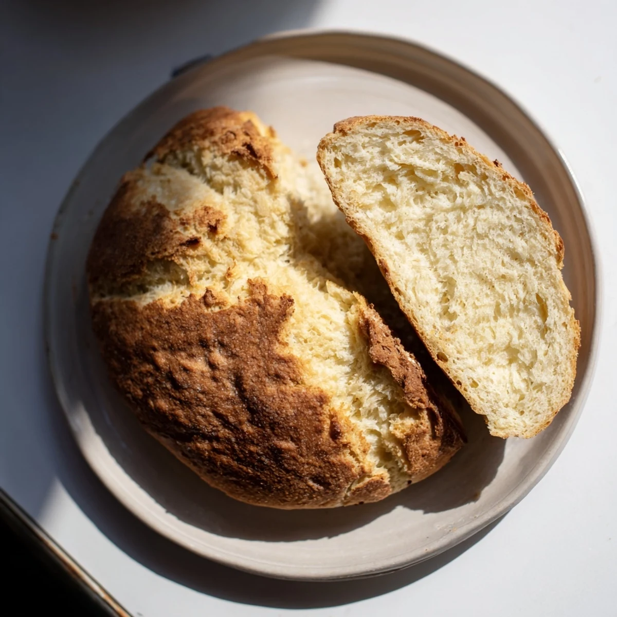 A close-up of Authentic 4-Ingredient Irish Soda Bread with a golden, rustic crust and tender crumb, sliced on a wooden board.