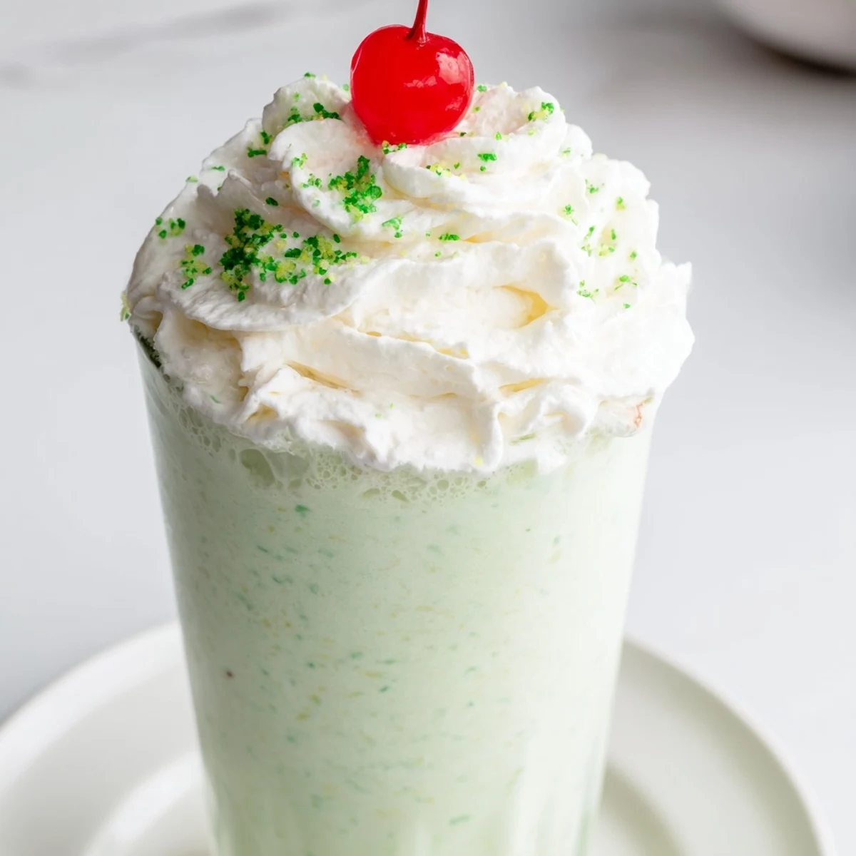 Tall glasses filled with vibrant green Homemade Copycat Shamrock Shake next to a blender and fresh ingredients for an easy St. Patrick's Day treat.