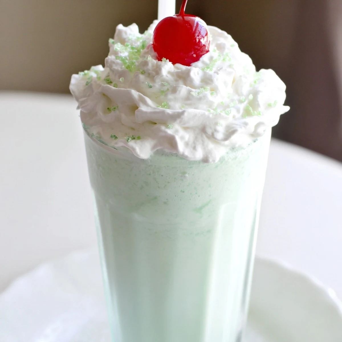 Serving two frosty glasses of creamy Homemade Copycat Shamrock Shake with whipped cream swirls and green sprinkles, ready to enjoy immediately.