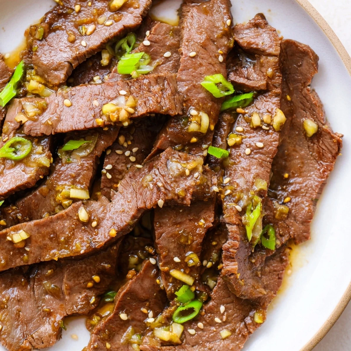 A close-up of Ultimate Slow Cooker Mongolian Beef in a slow cooker, glistening sauce with green onions and sesame seeds garnish.