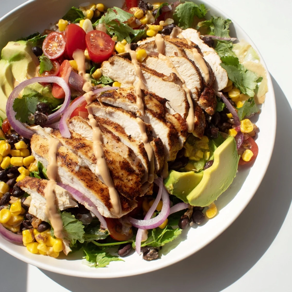 Sliced chipotle lime chicken salad with avocado, black beans, and fresh greens on a white plate.