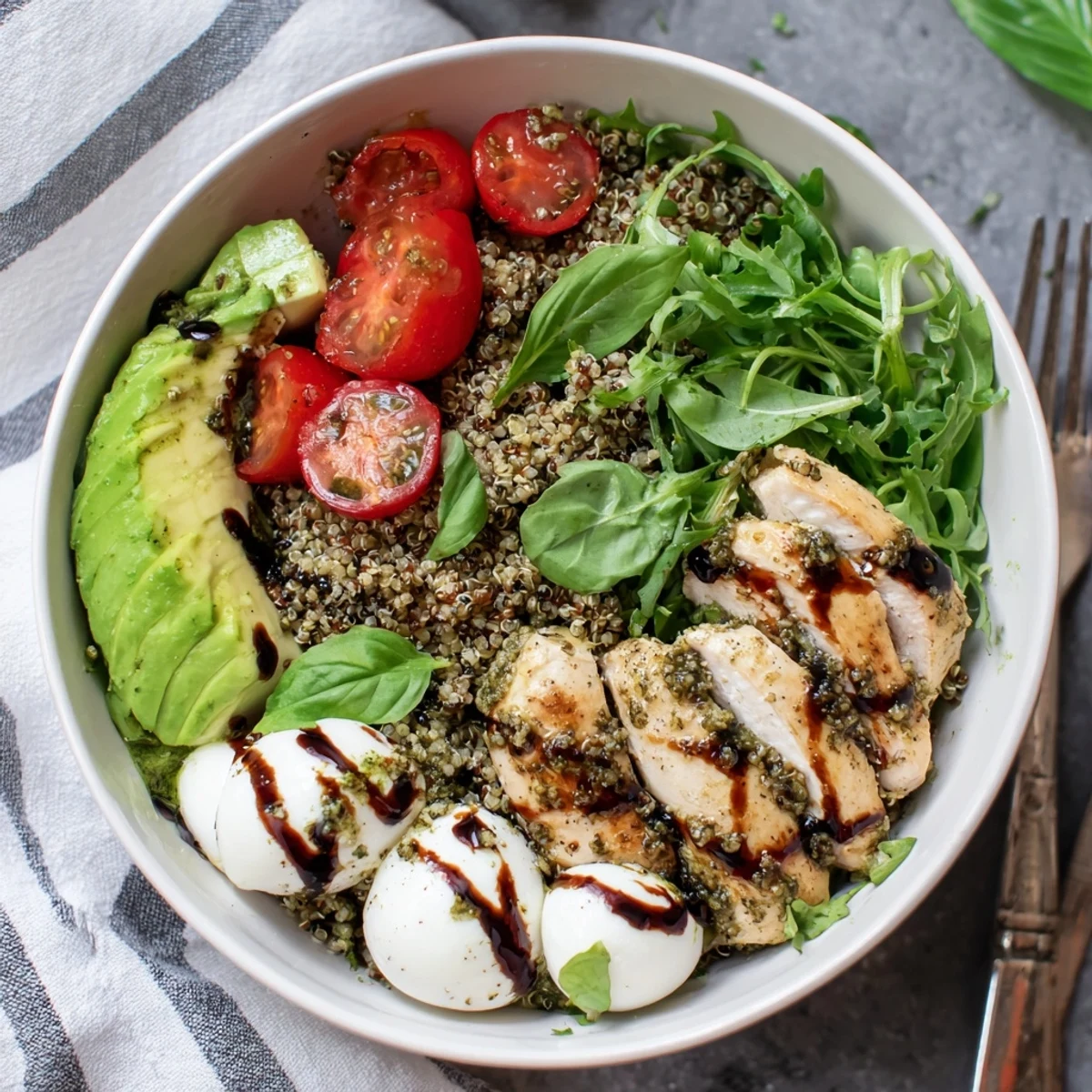 Fresh mozzarella, cherry tomatoes, and sliced avocado top the Pesto Chicken Caprese Grain Bowl, finished with balsamic drizzle.
