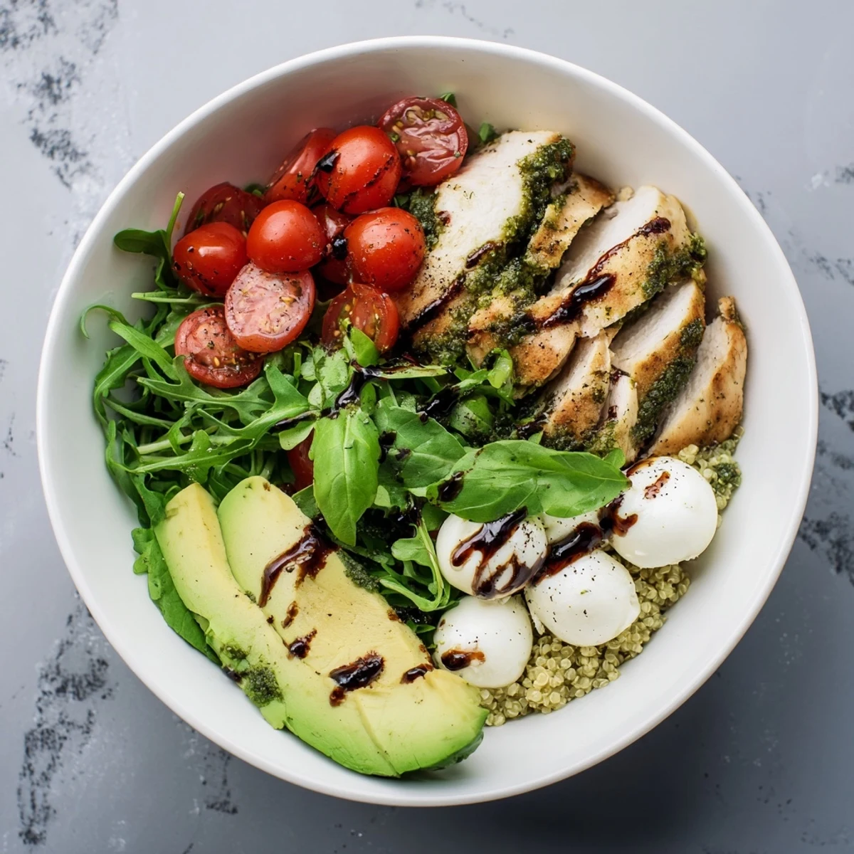 Sliced grilled chicken, basil, and creamy mozzarella shine in the colorful Pesto Chicken Caprese Grain Bowl on a bed of quinoa.