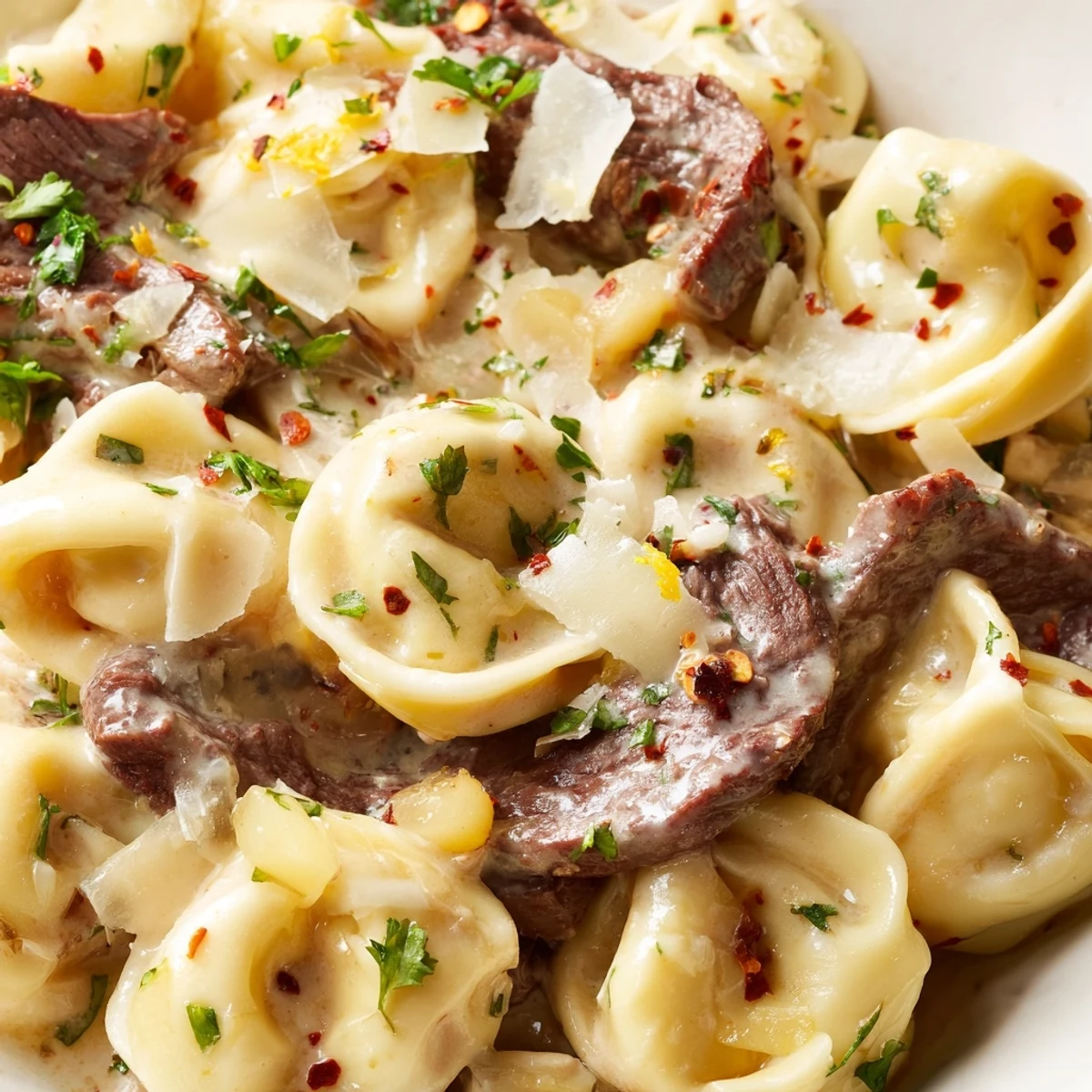 Plate of tender steak tortellini pasta swimming in a buttery garlic-herb cream sauce