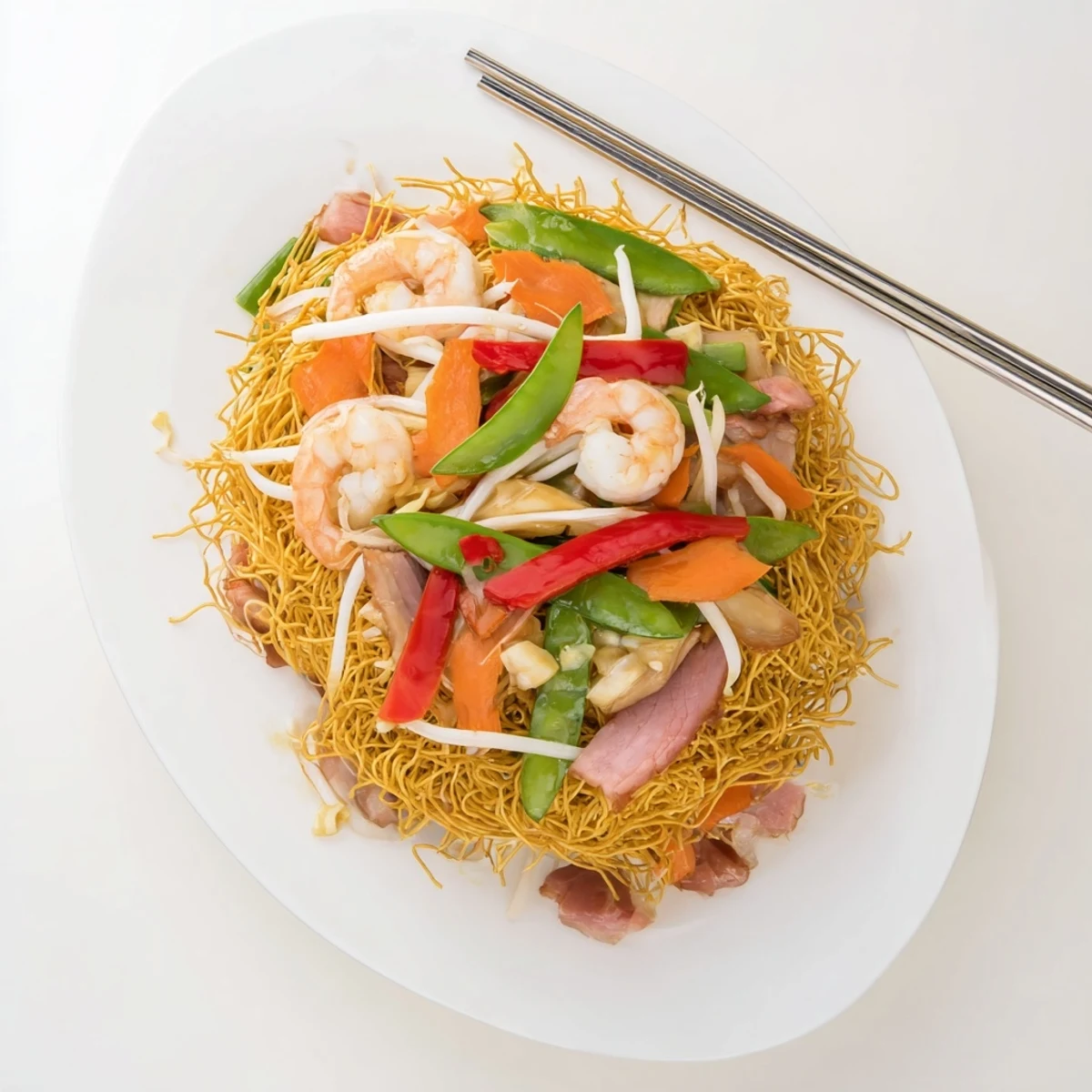 Steaming plate of Cantonese chow mein featuring crunchy noodles covered with colorful mixed vegetables and protein