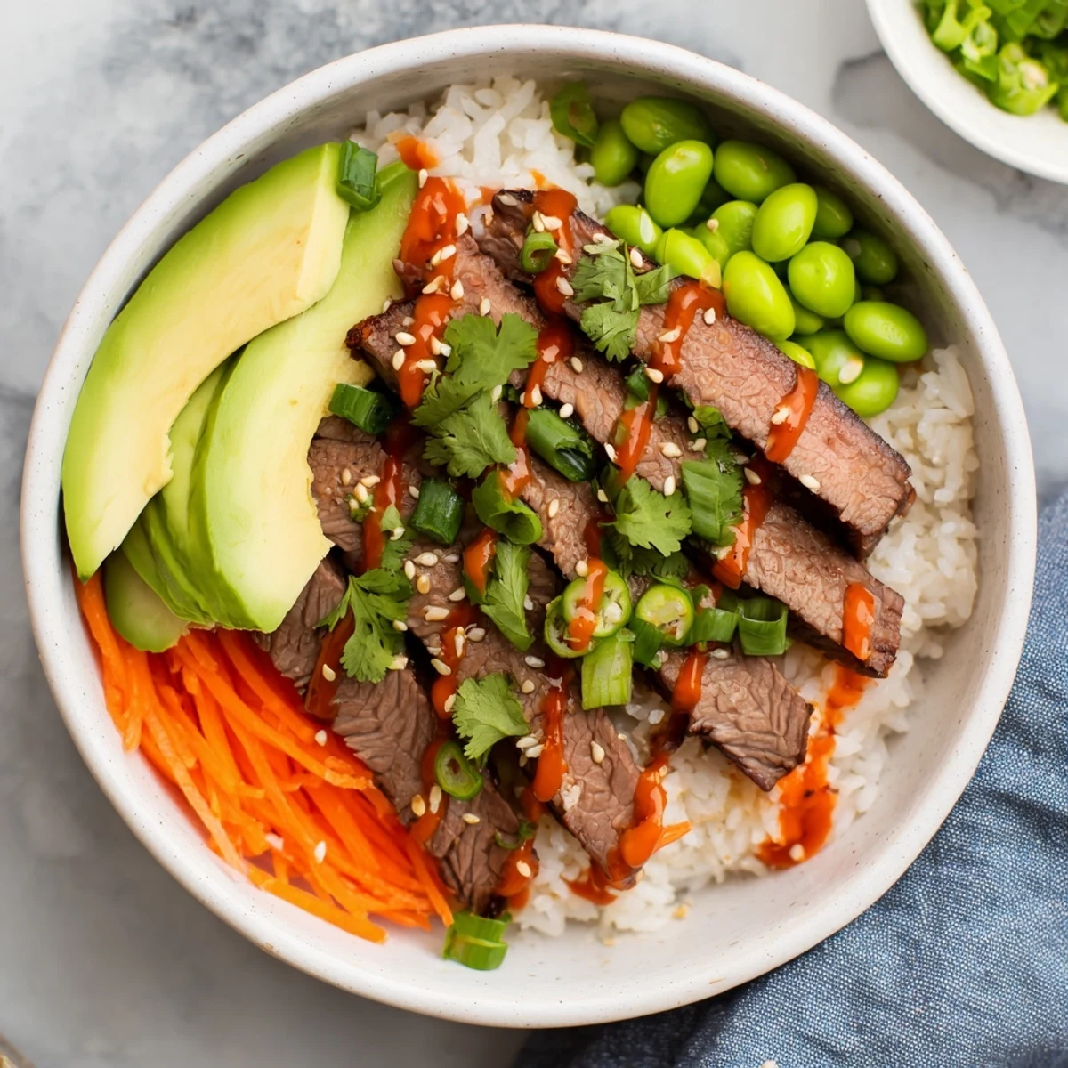 Savory marinated flank steak bowl featuring colorful vegetables, cilantro garnish, and creamy Sriracha drizzle atop steamed rice