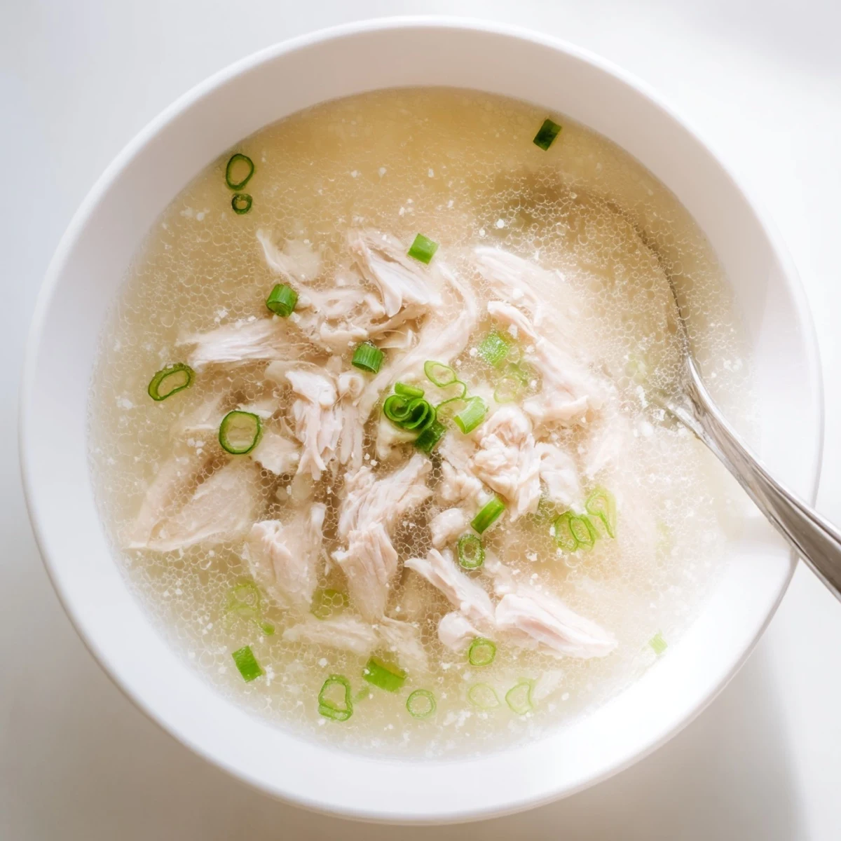 Golden bowl of Dakgomtang Korean chicken soup topped with fresh green onions and served with dipping sauce