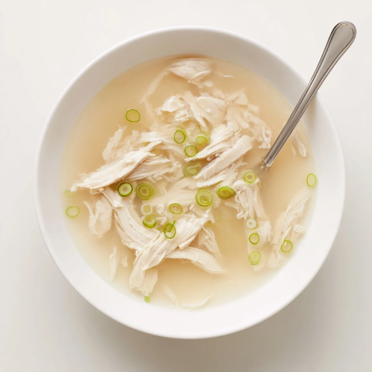 Comforting Dakgomtang soup featuring shredded chicken in clear broth garnished with scallions and sesame seeds