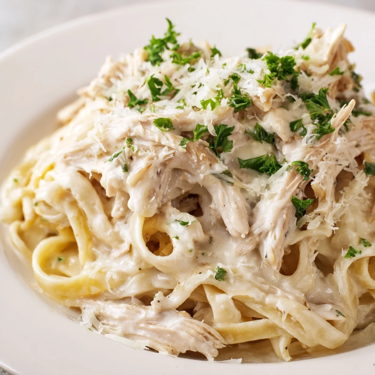 Homemade Crock Pot Chicken Alfredo bowl topped with chopped parsley displaying velvety cream sauce coating fettuccine pasta