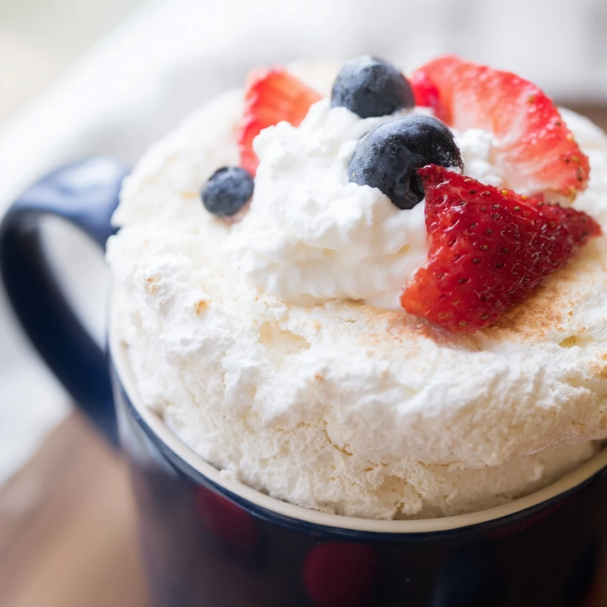 Single serving angel food cake rising in a mug with fluffy texture and golden-brown edges