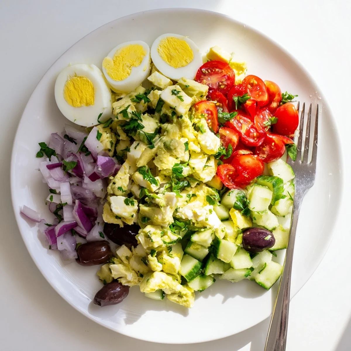 Creamy Mediterranean avocado egg salad with fresh vegetables and zesty lemon herb dressing in a serving bowl