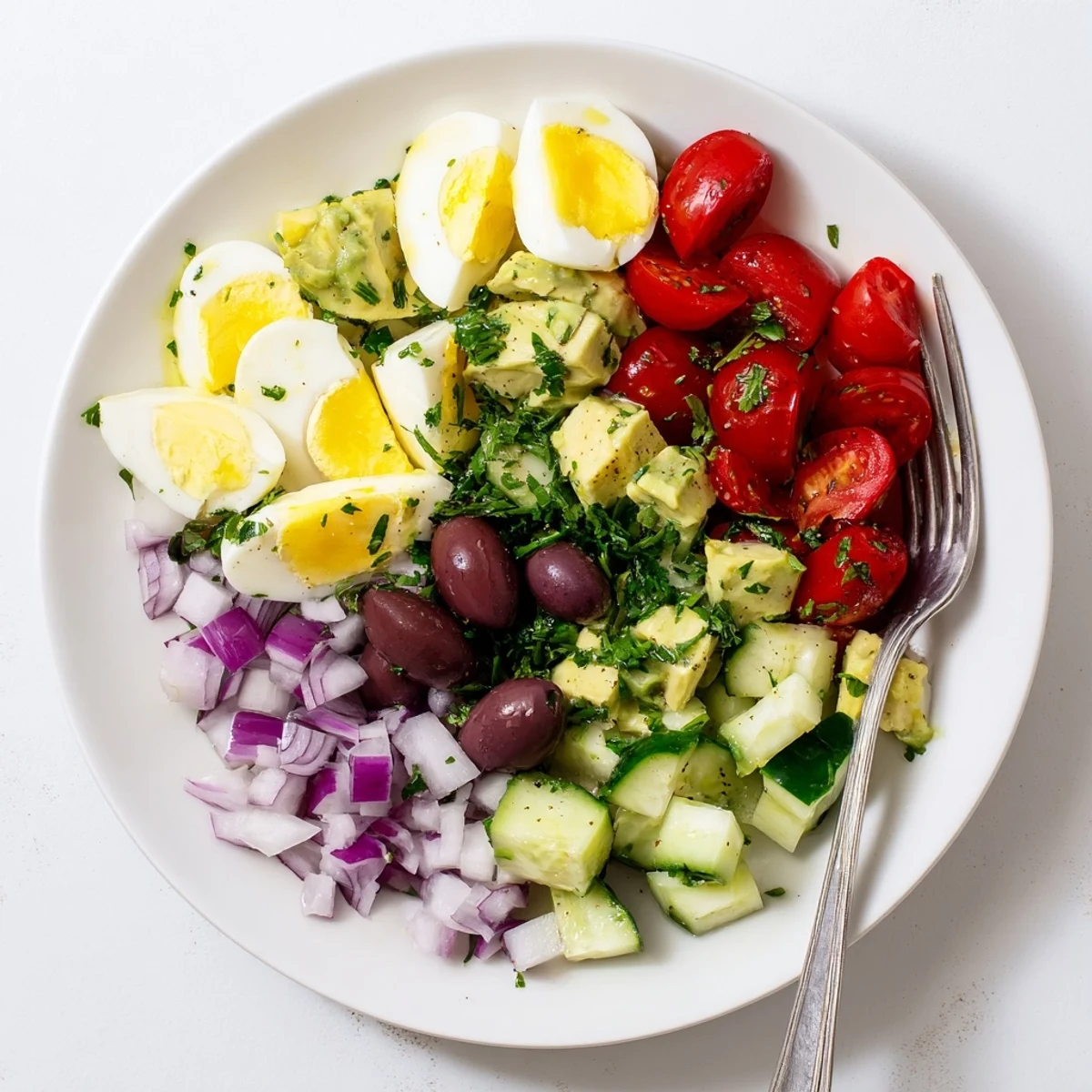 Vibrant green avocado egg salad plated with crisp red onion, colorful tomatoes and black Kalamata olives for a light lunch