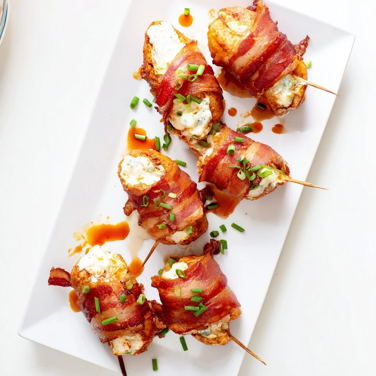 Bacon wrapped buffalo chicken bombs fresh from the oven with garnish and sauce drizzle