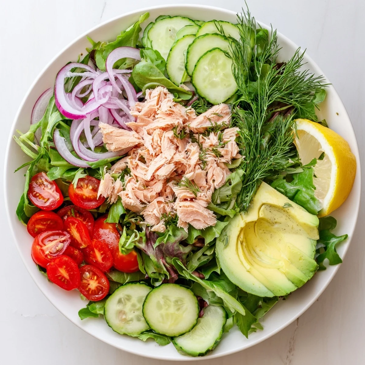 Flaked pink salmon pieces resting on crisp mixed greens with cherry tomatoes and creamy avocado slices in a minute salmon salad