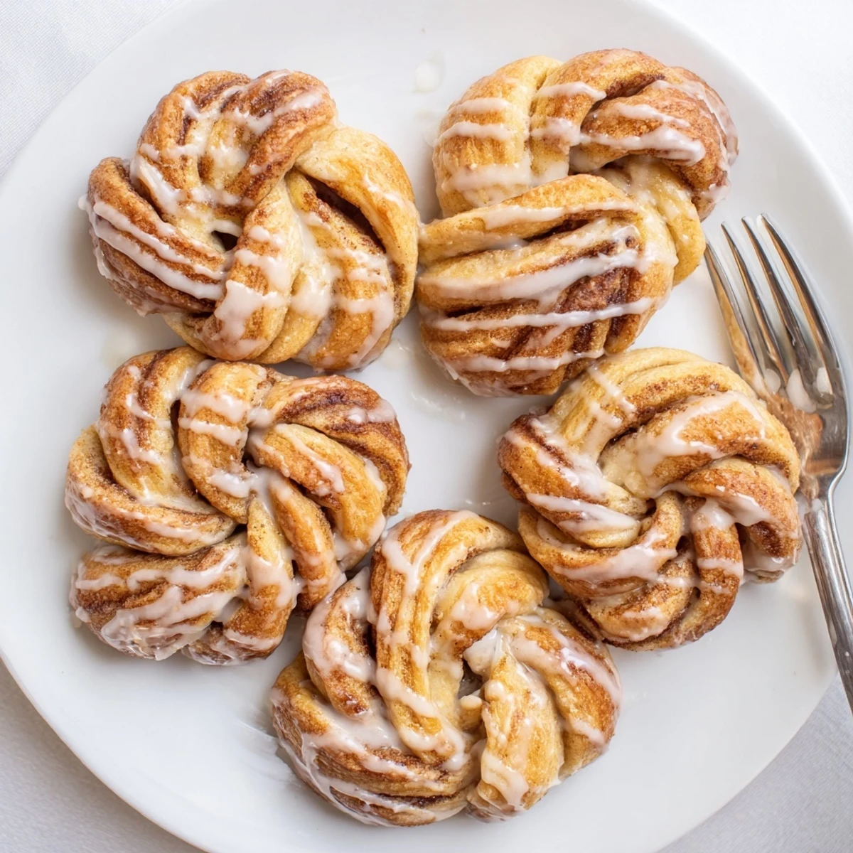 Soft glazed cinnamon twists arranged on white plate with powdered sugar dusting