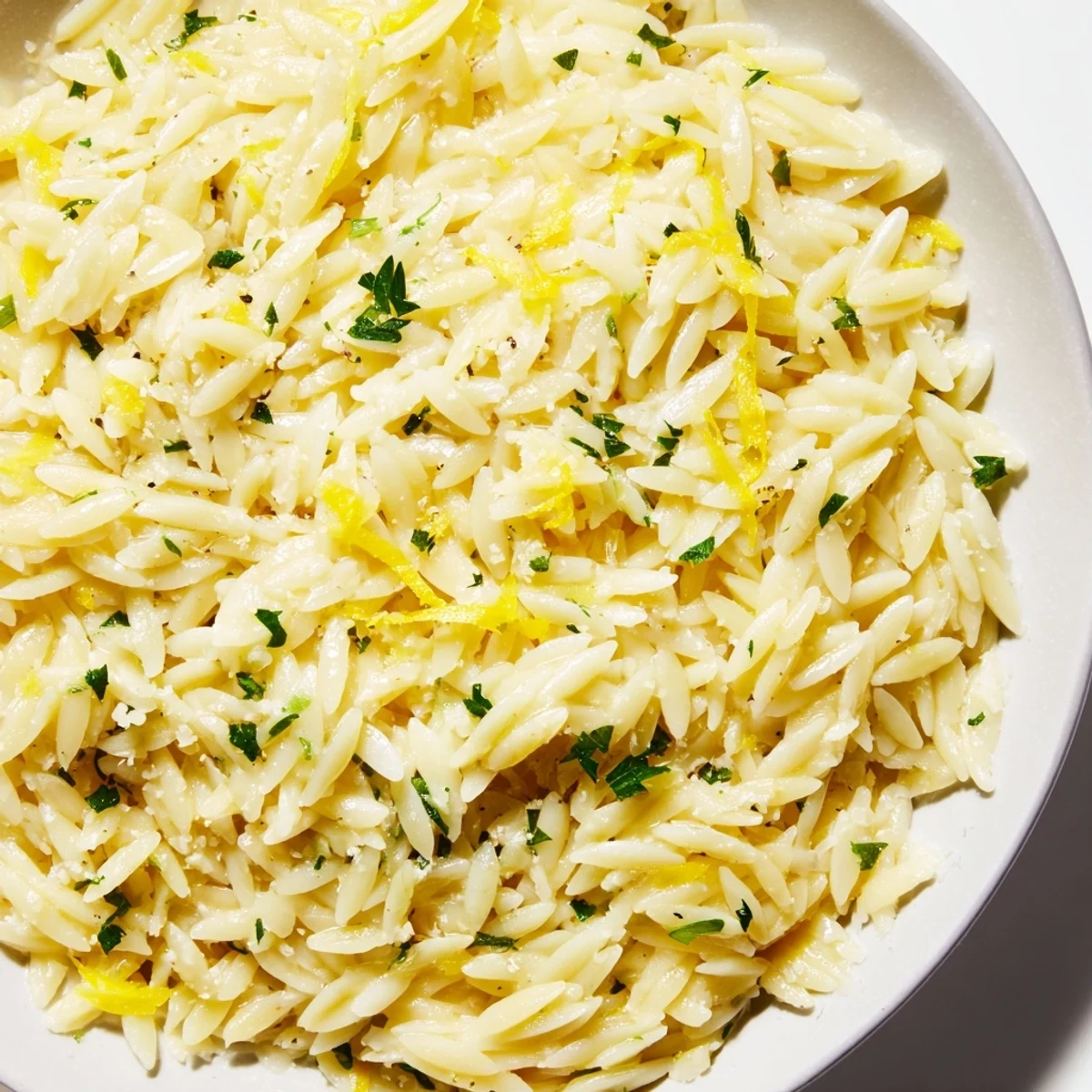 Golden lemon orzo pasta with fresh herbs and parmesan cheese in a white bowl