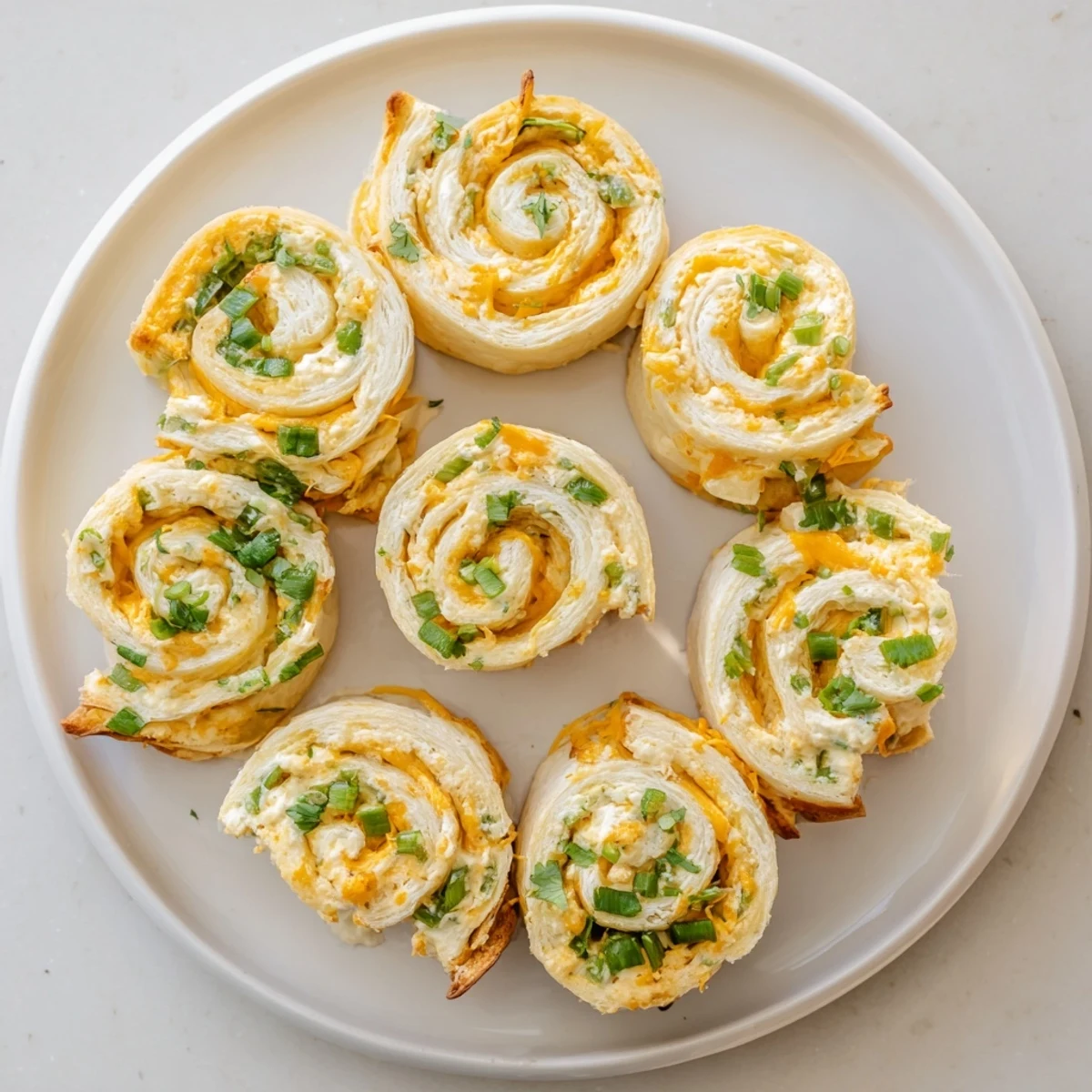 Golden baked jalapeno popper pinwheels arranged on a serving platter with fresh cilantro garnish