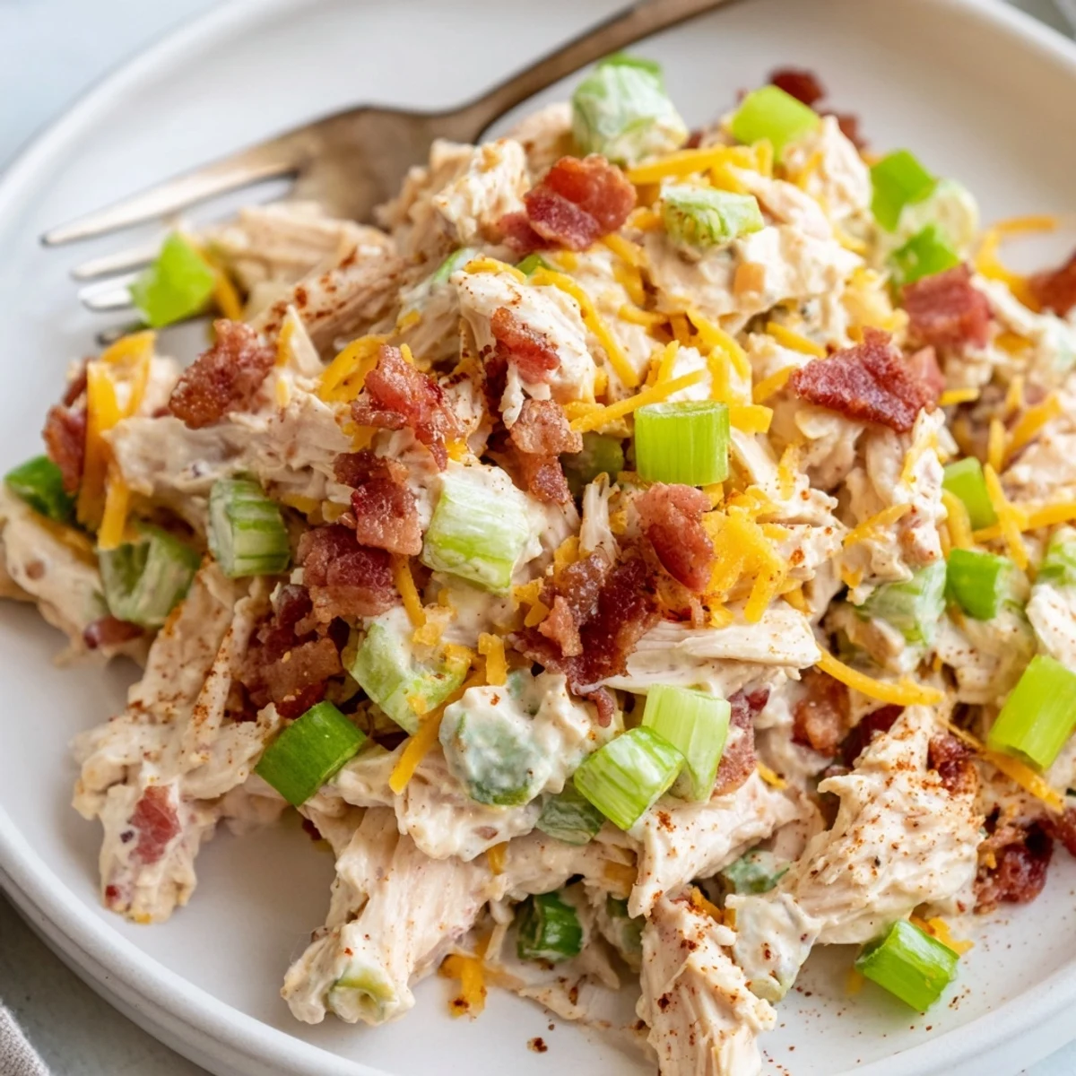 Spicy jalapeno popper chicken salad featuring tender shredded chicken, chopped peppers, and bacon crumbles on a rustic wooden board