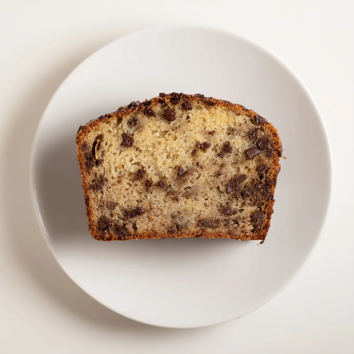 Golden chocolate chip banana bread loaf with melted chocolate chunks on a rustic wooden board