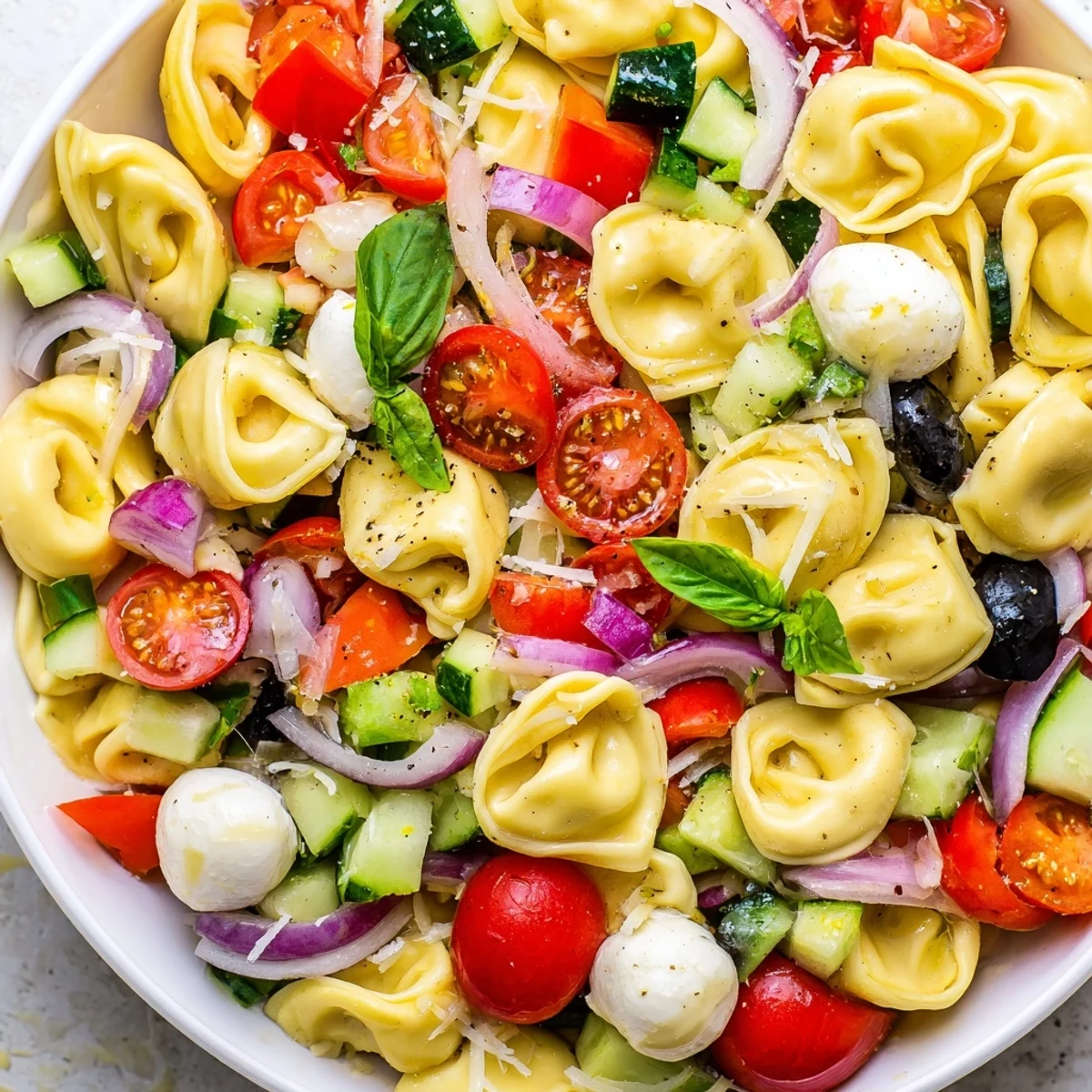 Cheese tortellini salad loaded with crisp vegetables and mozzarella, drizzled with herb dressing on a rustic table
