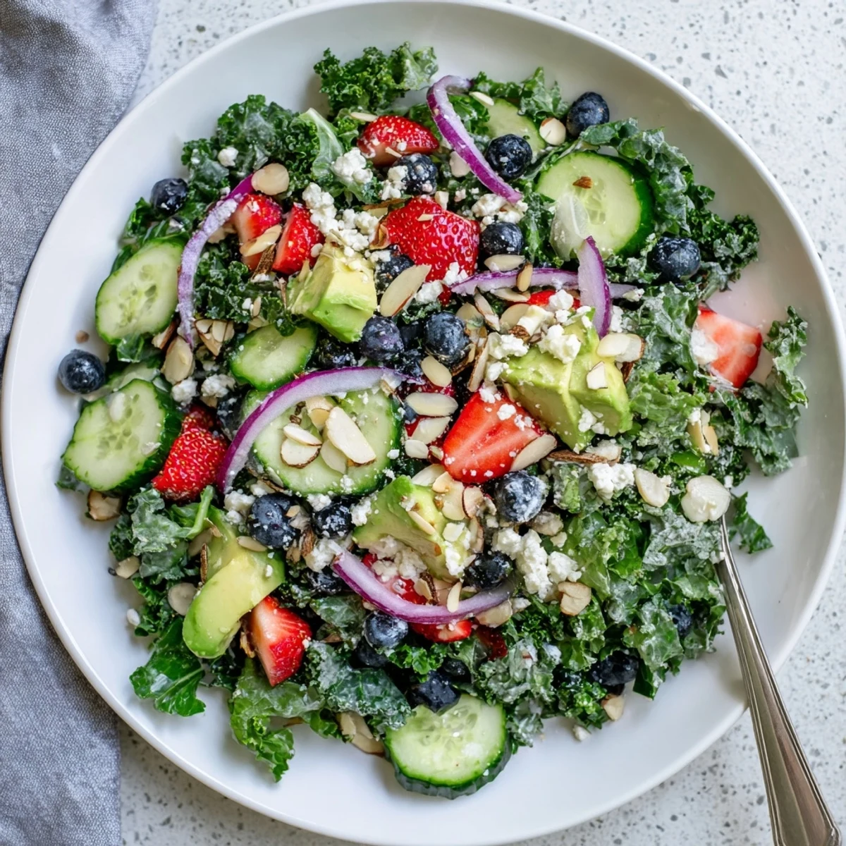 Colorful summer kale salad topped with feta, strawberries, and toasted almonds in a shallow bowl.