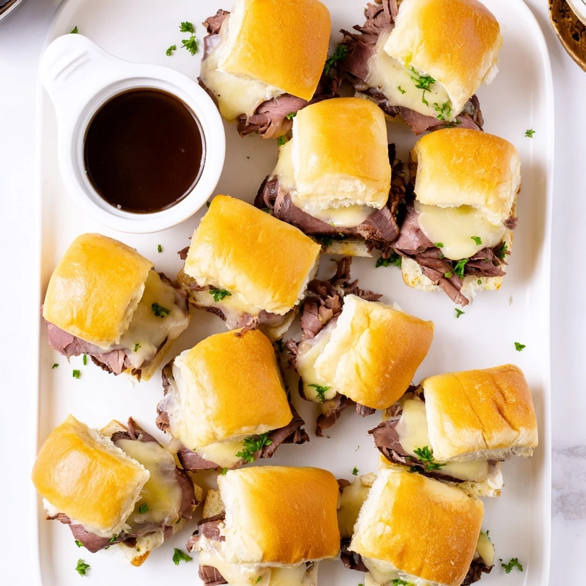 Baked French dip sliders piled high with savory roast beef, caramelized onions, and gooey cheese served alongside steaming cups of flavorful au jus