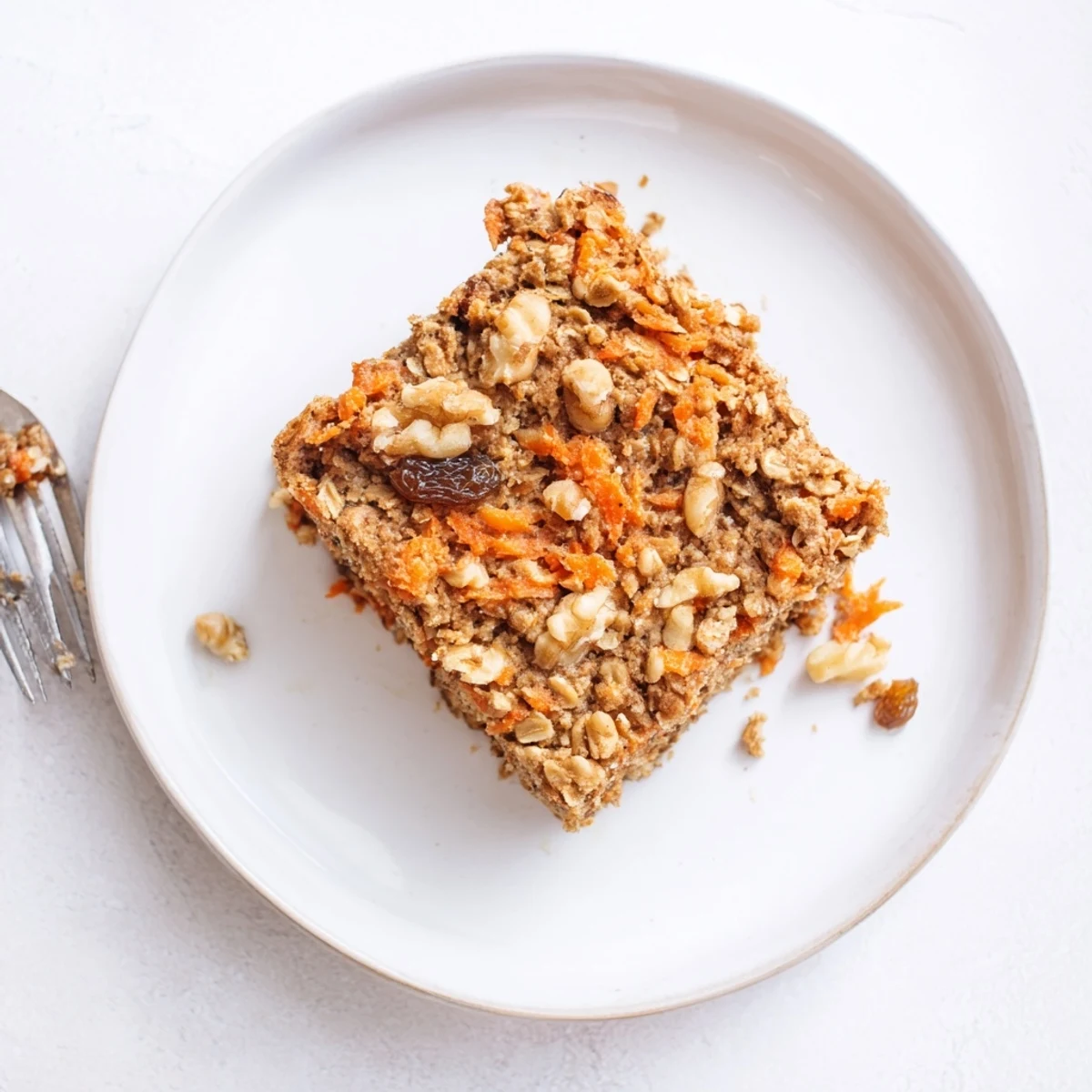 Moist flourless oatmeal carrot cake slice topped with cream cheese frosting and chopped walnuts on a white plate