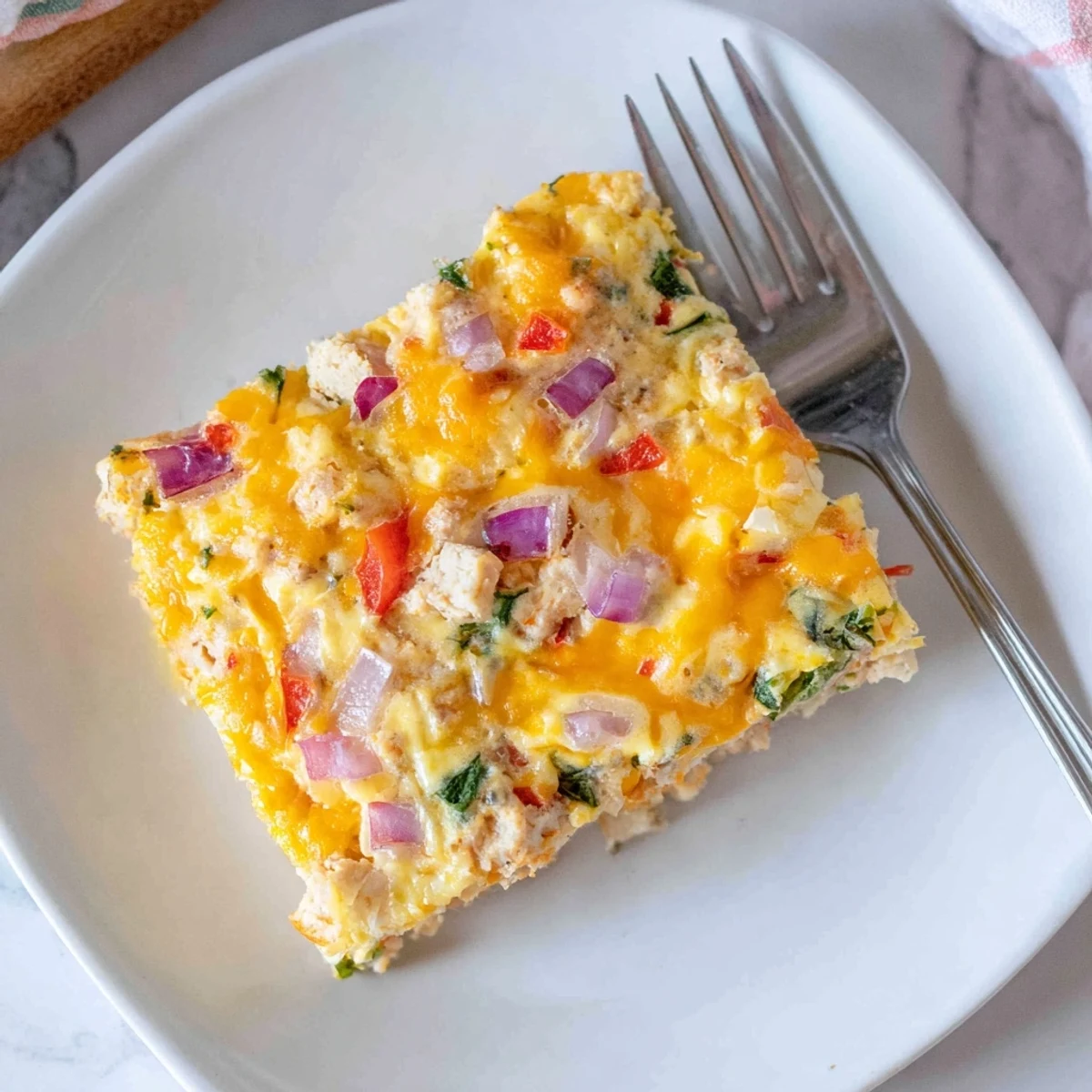 Slice of fluffy high protein egg casserole topped with cheese and vibrant diced vegetables