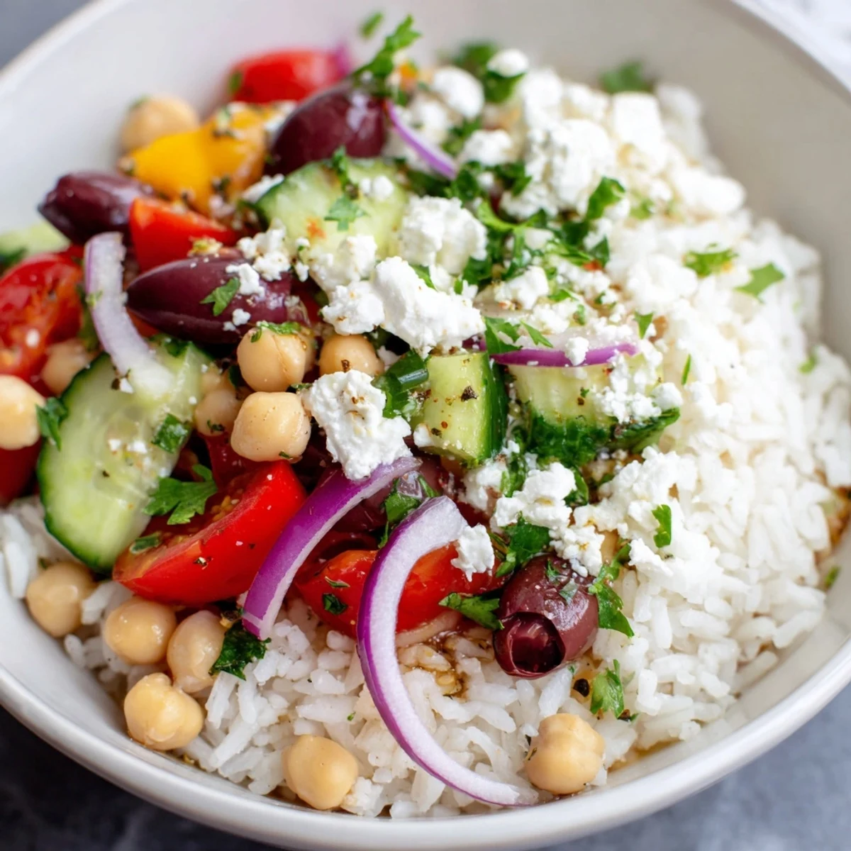 Colorful Mediterranean Rice Bowl topped with crisp cucumbers, juicy tomatoes, and crumbled feta cheese