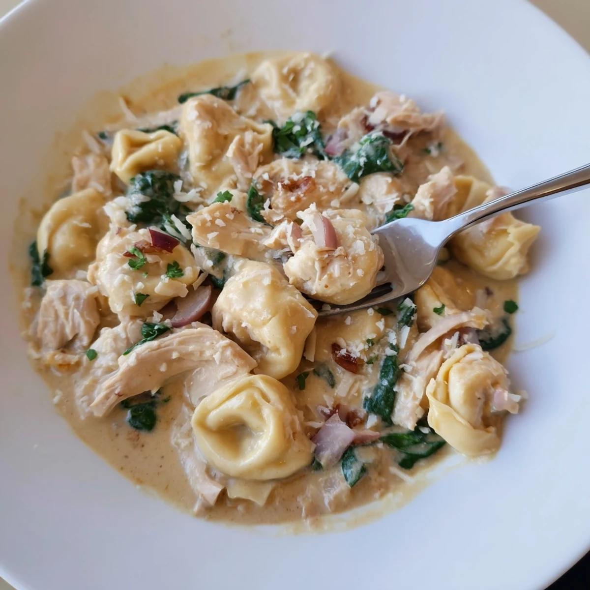 Creamy crockpot chicken tortellini soup with fresh spinach, parmesan, and parsley in a white bowl