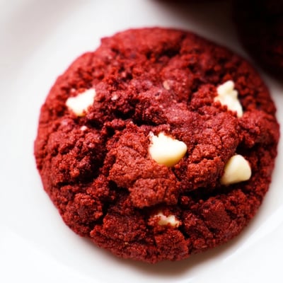 Freshly baked Red Velvet Cookies are stacked on a rustic wooden board for a homey dessert presentation.  