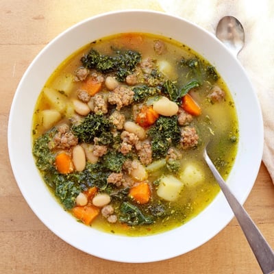 A vibrant bowl of Zuppa Toscana with Basil Pesto Lemon Broth topped with green pesto swirls and lemon zest.